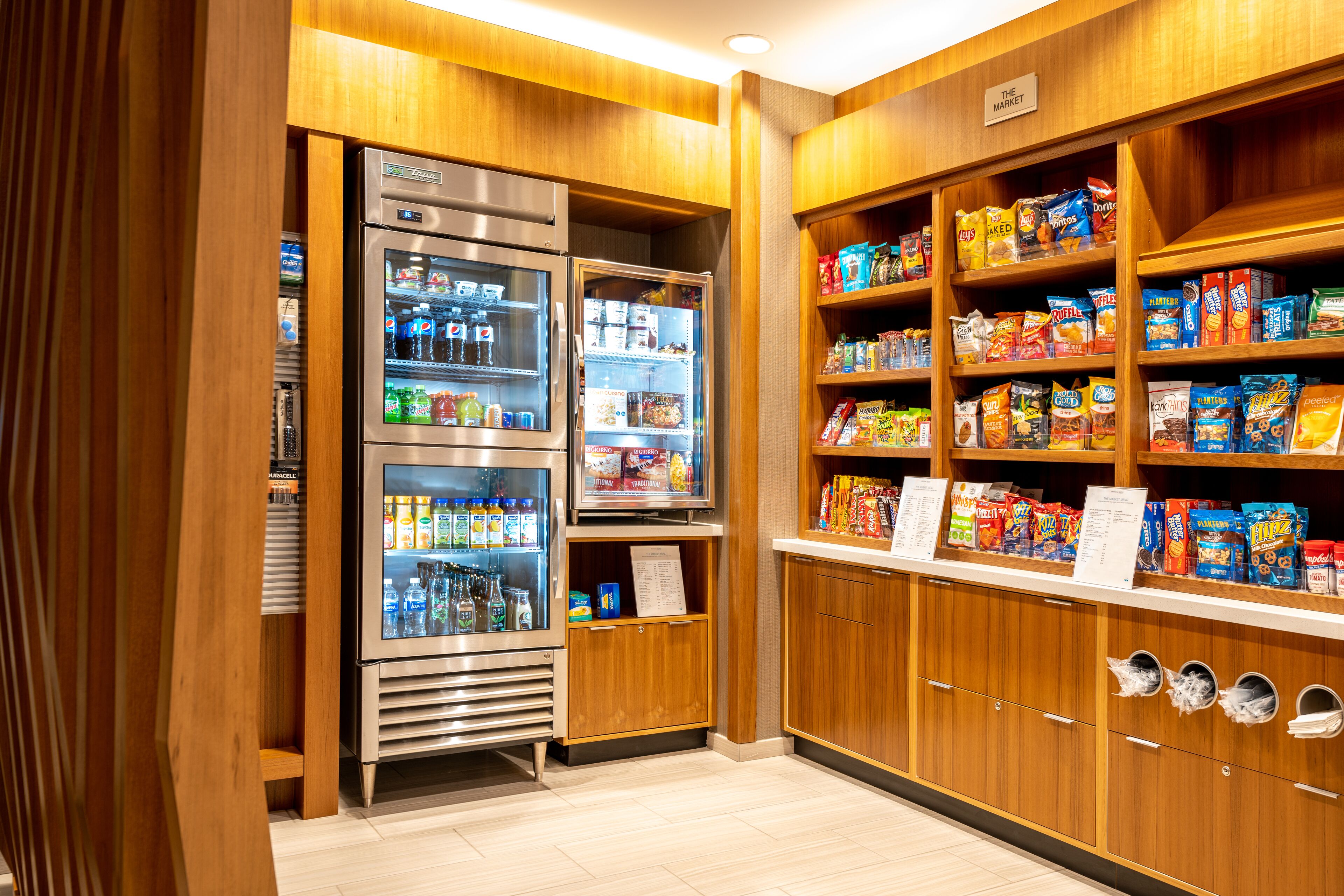Un quiosco autoservicio de refrigerios y bebidas, con varios dispensadores de bebidas refrigeradas y estantes llenos de diferentes snacks y productos envasados.