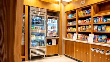 Un quiosco autoservicio de refrigerios y bebidas, con varios dispensadores de bebidas refrigeradas y estantes llenos de diferentes snacks y productos envasados.
