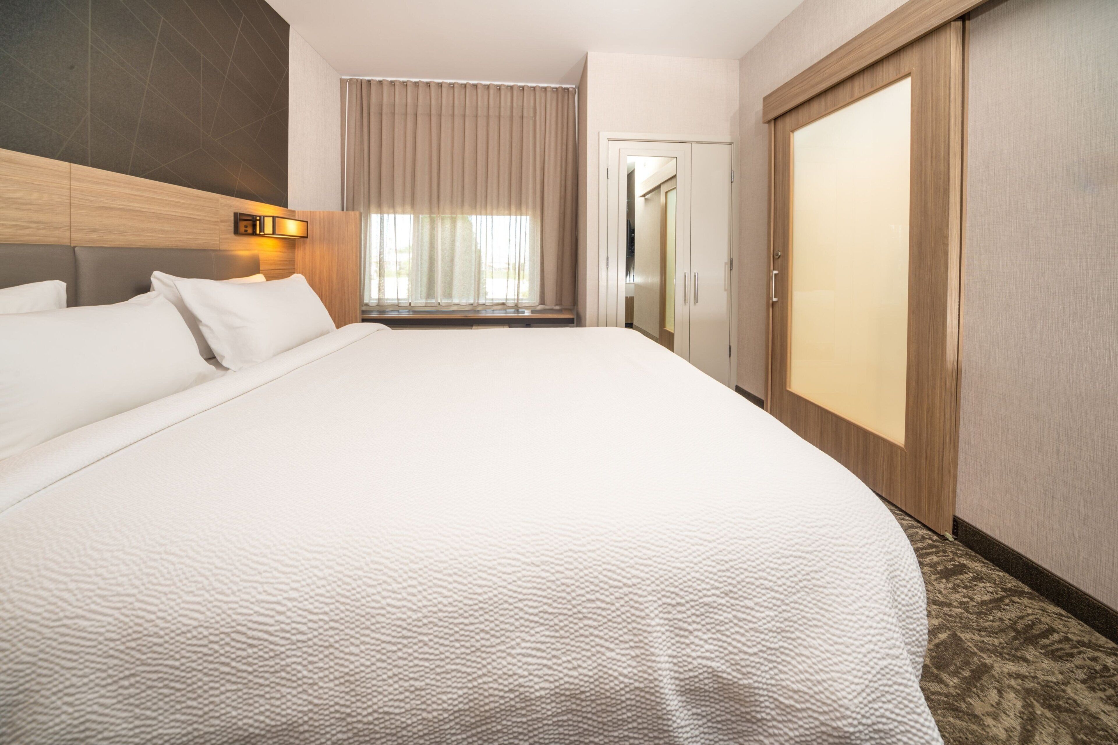 Hotelkamer met een groot bed, een kledingkast, een raam met gordijnen en een wandlamp.