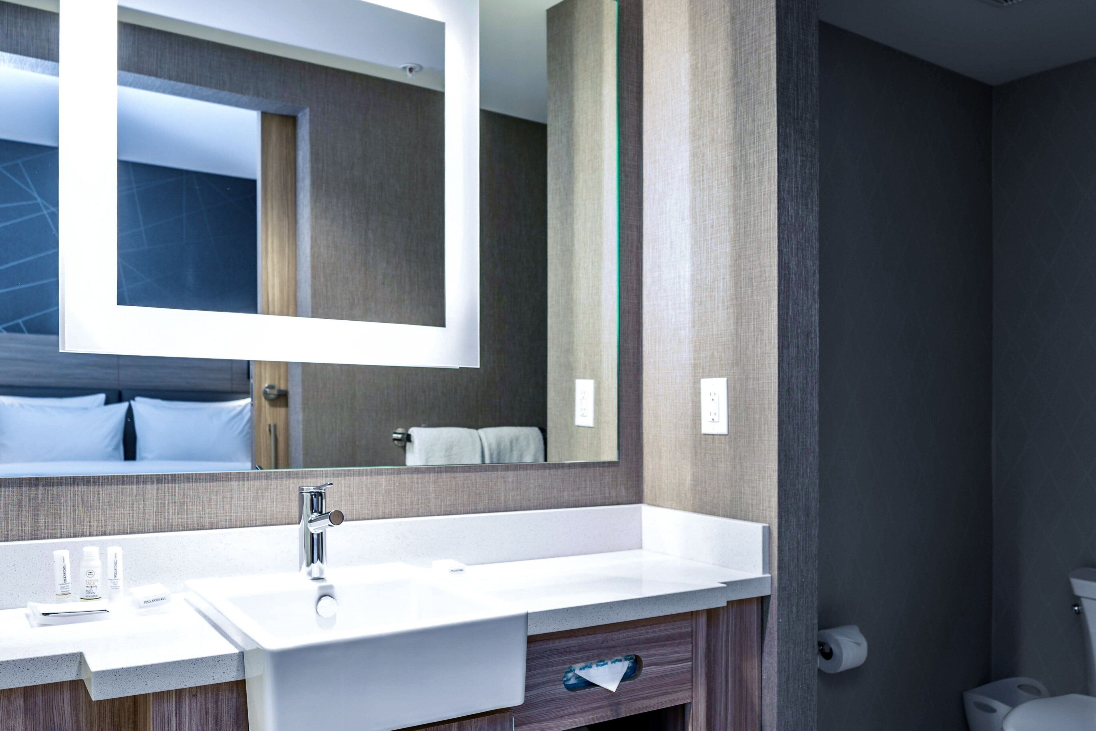Un baño moderno con un espejo grande, lavamanos blanco y tocador de madera.