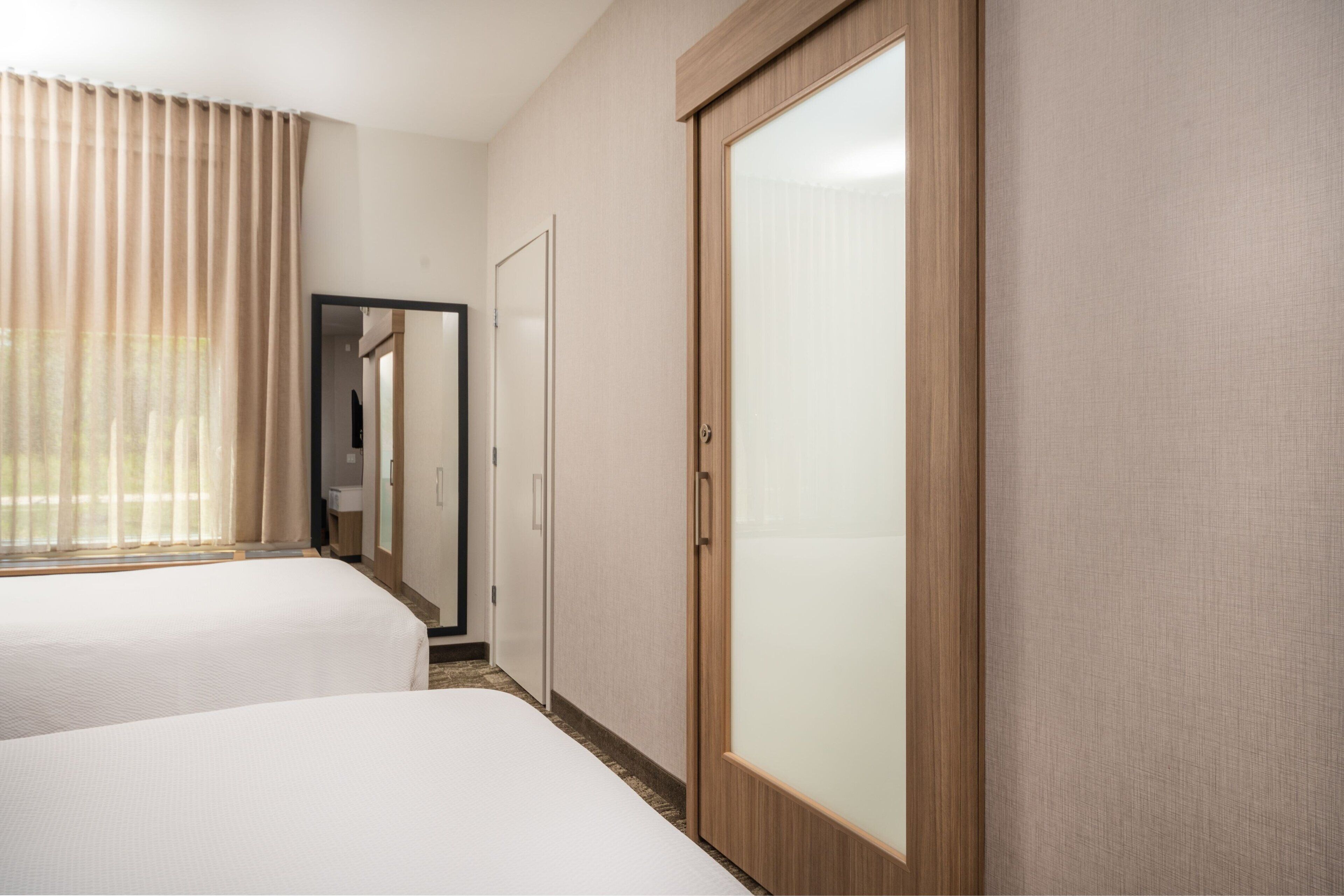 A hotel room with two beds, a wardrobe, and a mirror.