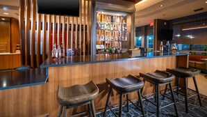 A bar area with a wooden counter, bar stools, and a shelf with various bottles. - SpringHill Suites by Marriott Kenosha (Kenosha)