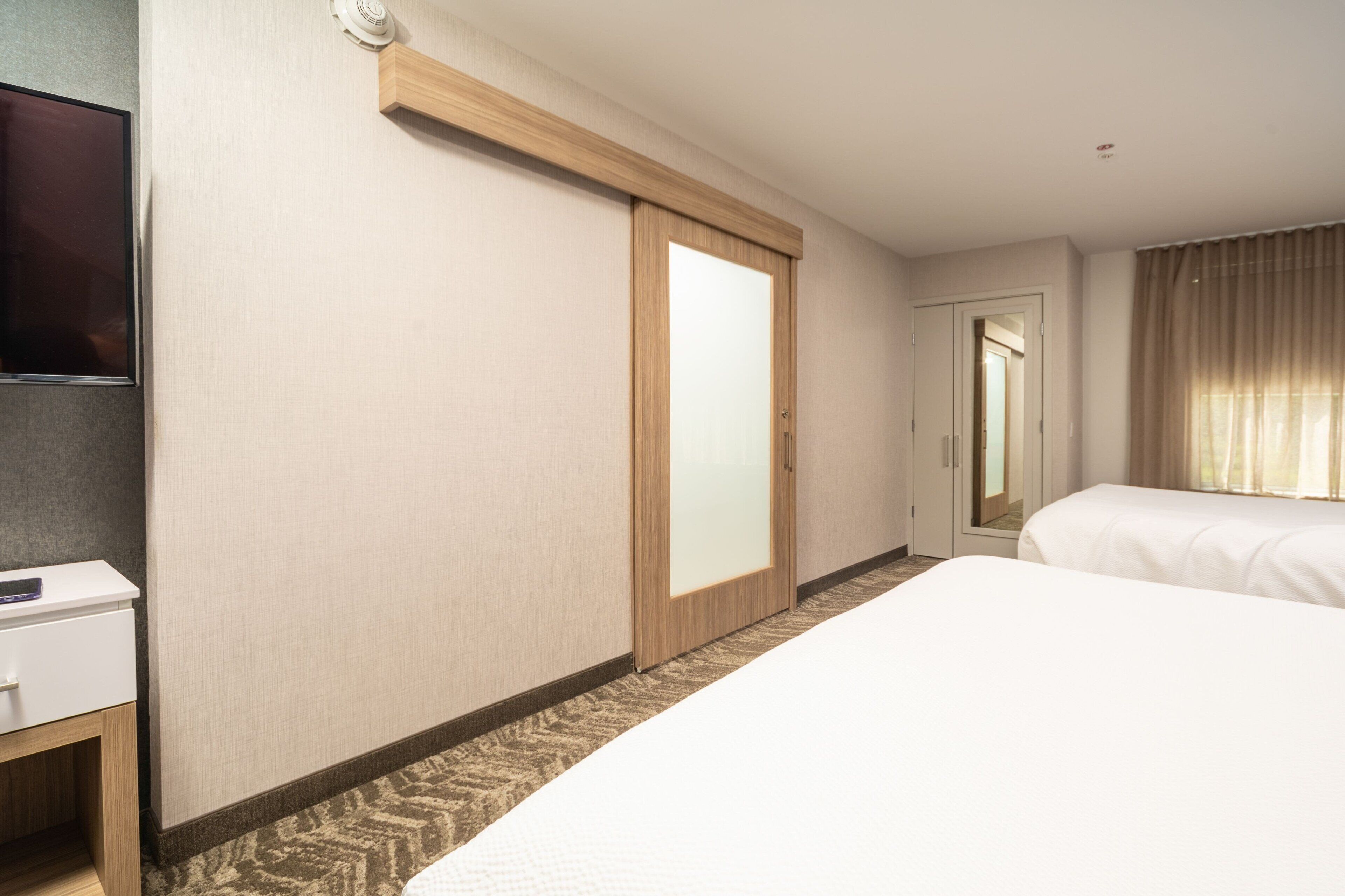 A hotel room with a bed, a desk, a television, a sliding door, and a window with curtains.