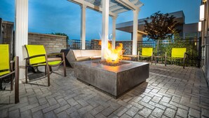 A fire pit with chairs around it, a pergola, and a brick wall in the background. - SpringHill Suites by Marriott Kenosha (Kenosha)