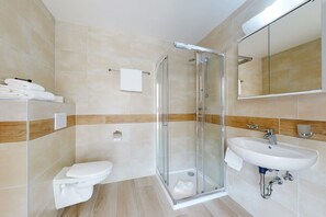 Un baño moderno con ducha de vidrio, un lavabo blanco y un inodoro.