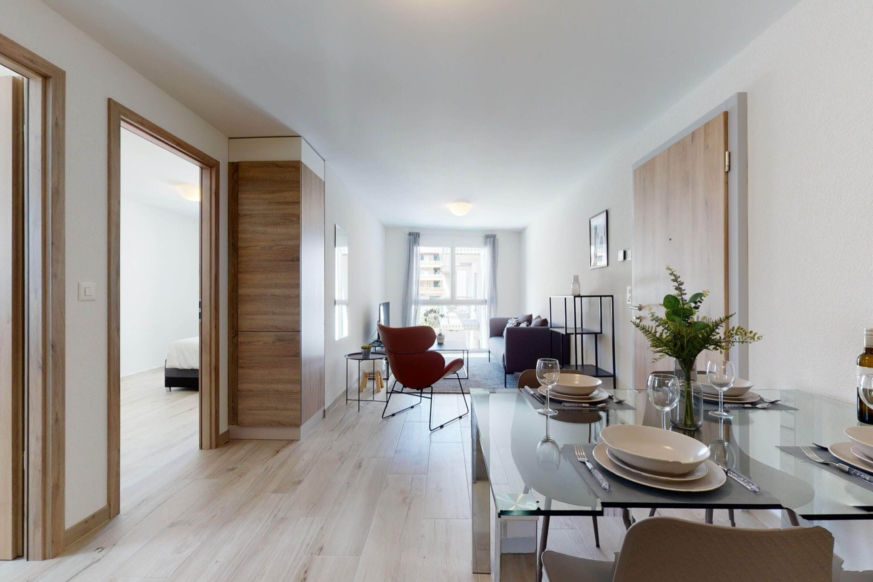 Un comedor moderno con una mesa de vidrio, sillas rojas y vista al salón.