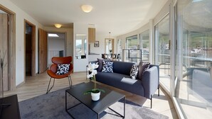 A modern living room with a sofa, a coffee table, and a chair. There is a large window offering a view of the outdoors. - Nonanteneuf Aigle (Aigle)
