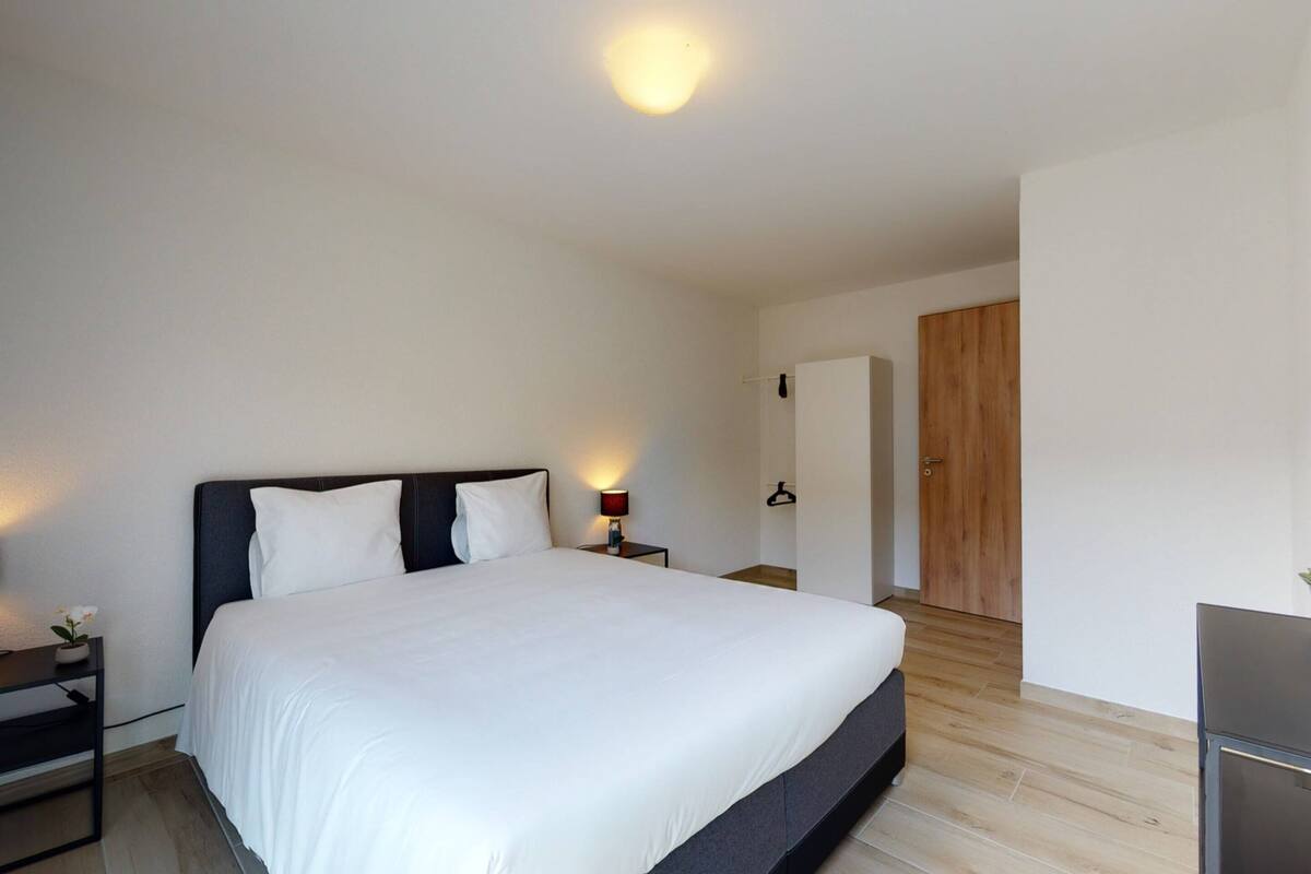 A modern bedroom with a large bed, a bedside table with a lamp, and a wardrobe.