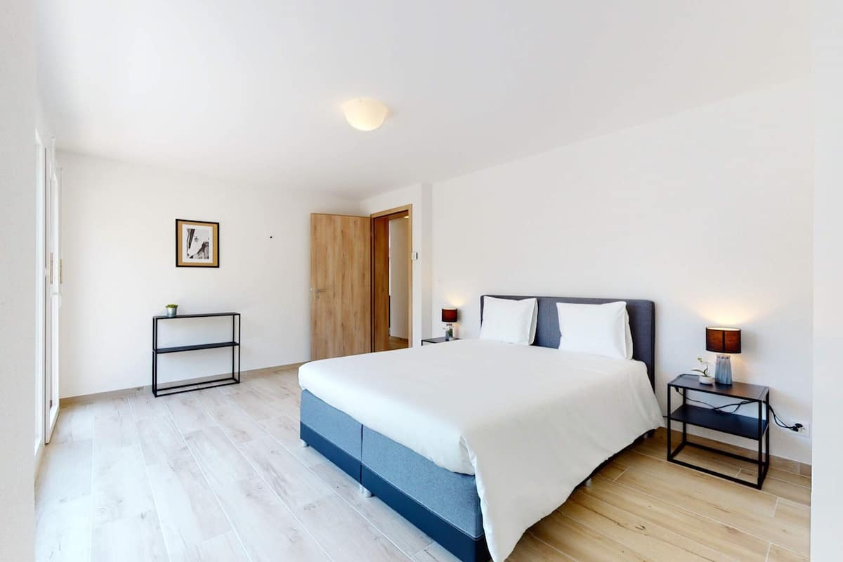 A bedroom with a large bed, bedside tables, a wooden wardrobe, and a small shelf.