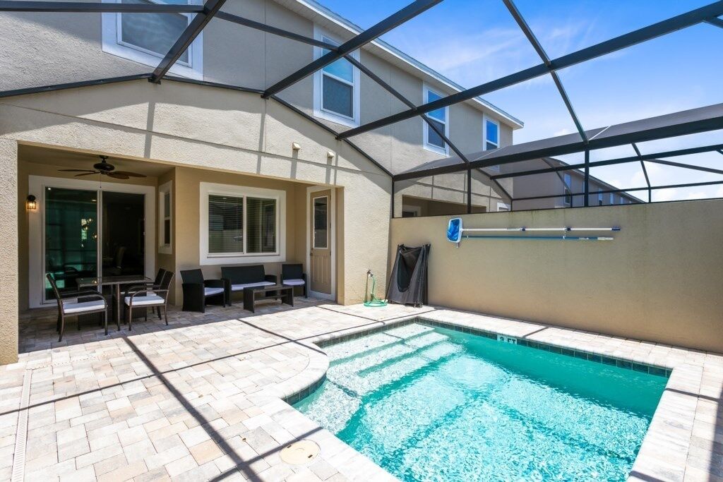 A backyard with a swimming pool, patio furniture, and a covered seating area.