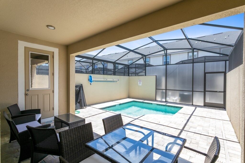 Un patio cubierto con piscina, mobiliario exterior y una mesa de vidrio.