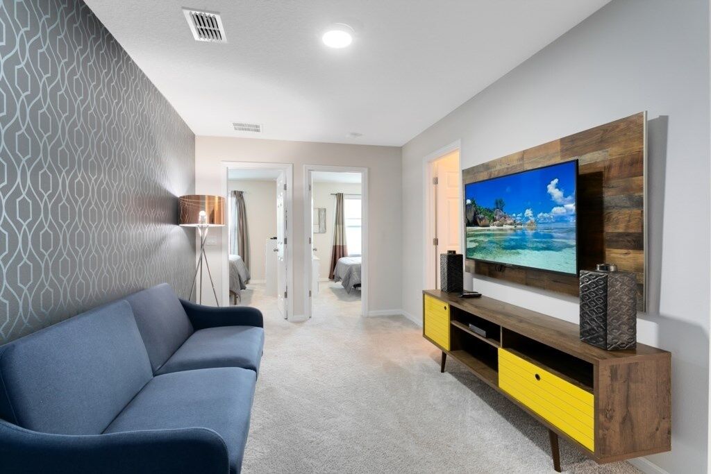 A modern living room with a large flat-screen TV mounted on a wooden TV stand, a blue sofa, and a patterned wall.