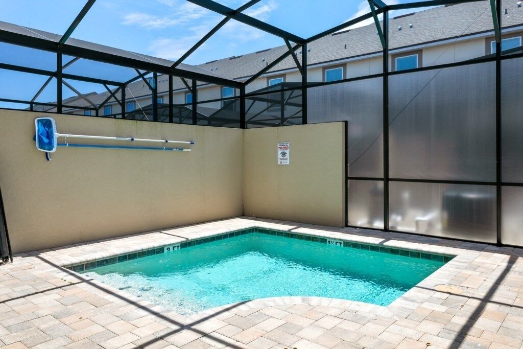 Una piscina con techo de vidrio, rodeada por un muro color beige y una valla metálica.