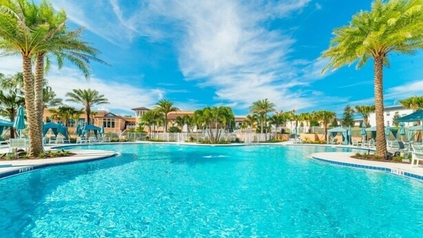 Una piscina azul cristalina rodeada de palmeras y sillas de descanso, con edificios al fondo.