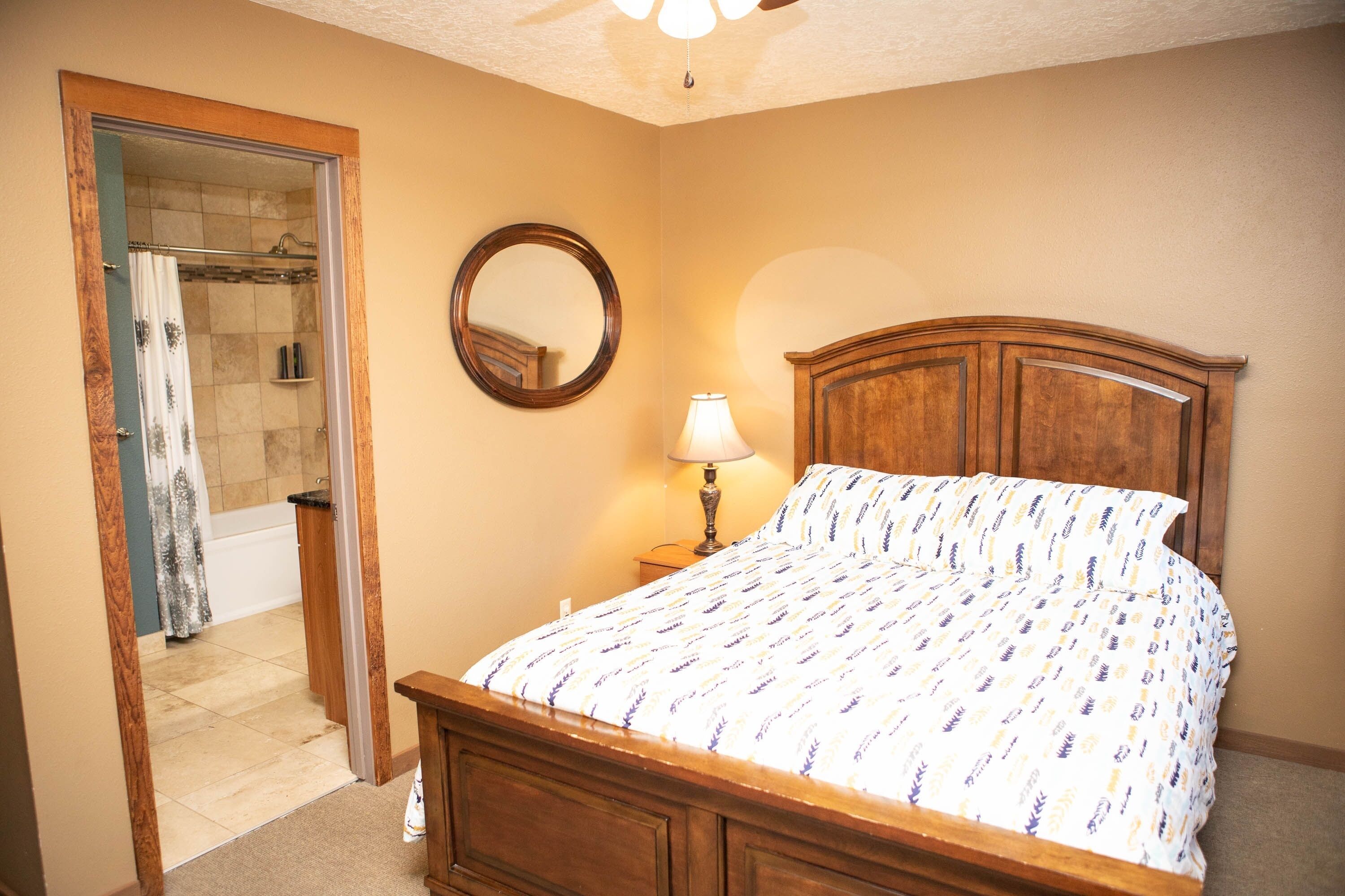 A bedroom with a wooden bed, a round mirror, a nightstand with a lamp, and a shower area with a curtain.