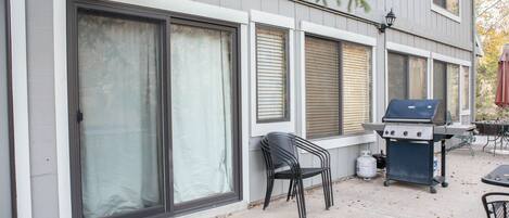 Una terrazza con una griglia, sedie e una porta con una finestra.