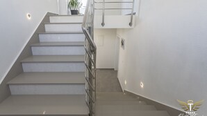 En moderne trappe med gelænder i metal, hvide vægge og en potteplante øverst.