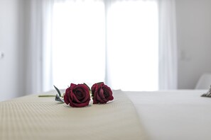 Un lit recouvert d’une courtepointe blanche, avec deux roses rouges posées dessus.