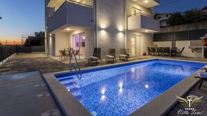 En moderne bygning i to etager med swimmingpool, udendørs siddepladser og en velbelyst indgang.