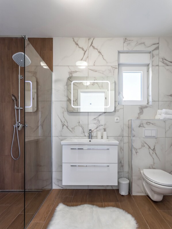 Une salle de bain moderne avec une douche à parois de verre, un meuble-lavabo blanc avec un miroir et des toilettes.