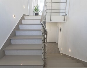 A modern staircase with a metal railing, white walls, and a potted plant at the top.
