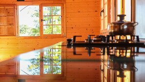 Interior de una cabaña de madera con un ventanal grande, una estufa y un reflejo en el suelo.