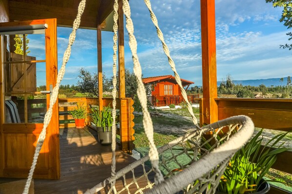 A wooden deck with a hammock, potted plants, and a view of a red building in the distance.