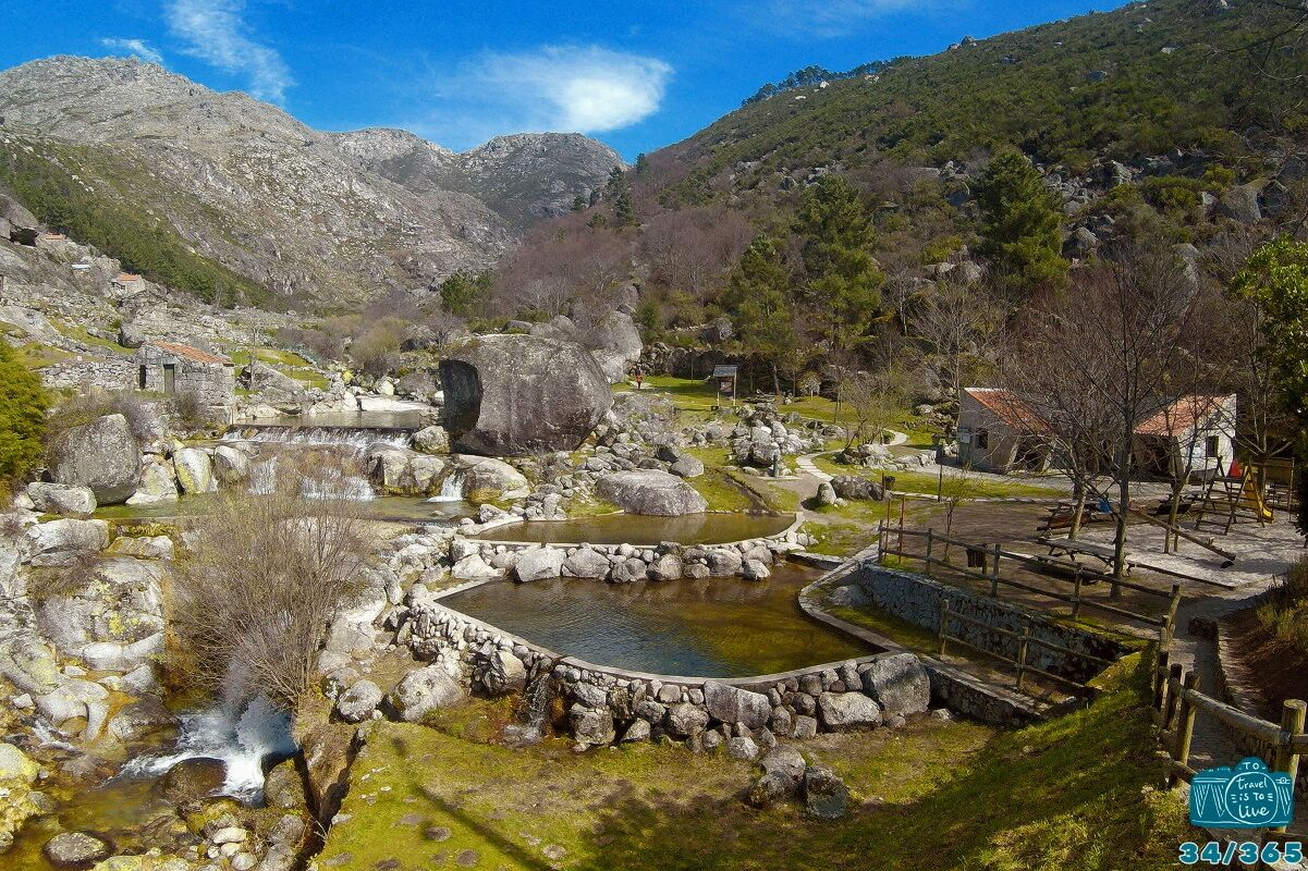 A mountainous landscape with a small pond, stone structures, and a wooden bridge.