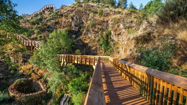 Un paseo marítimo de madera con barandillas que asciende por una ladera rocosa con vegetación escasa.