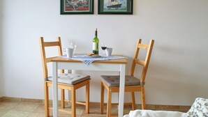 A small dining area with a white table and two wooden chairs, a bottle of wine, and two glasses. - Kuschelige Butze an der Ostsee (Heringsdorf)