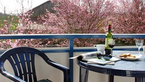 A table with a bottle of wine, glasses, a plate of cookies, and a chair on a balcony with a view of blooming trees. - Kuschelige Butze an der Ostsee (Heringsdorf)