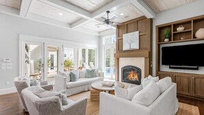 A spacious living room with a fireplace, white sofas, and a flat-screen TV mounted on the wall. - Luxury Home w/ Private Heated Pool in Seagrove! (Santa Rosa Beach)