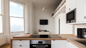 A modern kitchen with a wooden countertop, built-in oven, and a flat-screen TV mounted above the counter. - Immaculate 1-Bed Apartment on Hove Seafront (Hove)