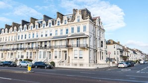 A row of traditional terraced houses with multiple stories, a clear sky, and parked cars along the street. - Immaculate 1-Bed Apartment on Hove Seafront (Hove)