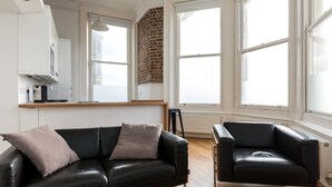 A modern living room with a black leather sofa, a black leather armchair, and a wooden floor. - Immaculate 1-Bed Apartment on Hove Seafront (Hove)