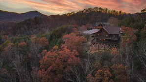 A wooden cabin with a deck, surrounded by autumn foliage and hills.