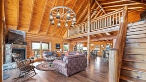 A spacious log cabin interior with a fireplace, wooden furniture, and a balcony.