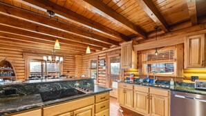 A log cabin kitchen with wooden cabinets, a granite countertop, and pendant lighting.
