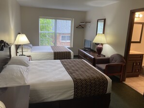 A hotel room with two beds, a desk with a TV, a chair, a mirror, and a window with blinds. - Hotel Pratt in the heart of Cooperstown, New York **Baseball Central** (Cooperstown)