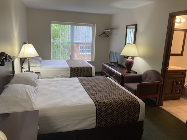 A hotel room with two beds, a desk with a TV, a chair, a mirror, and a window with blinds.
