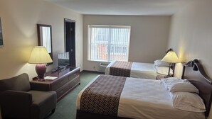 A hotel room with two beds, a desk, a chair, a TV, and a window with blinds. - Hotel Pratt in the heart of Cooperstown, New York **Baseball Central** (Cooperstown)
