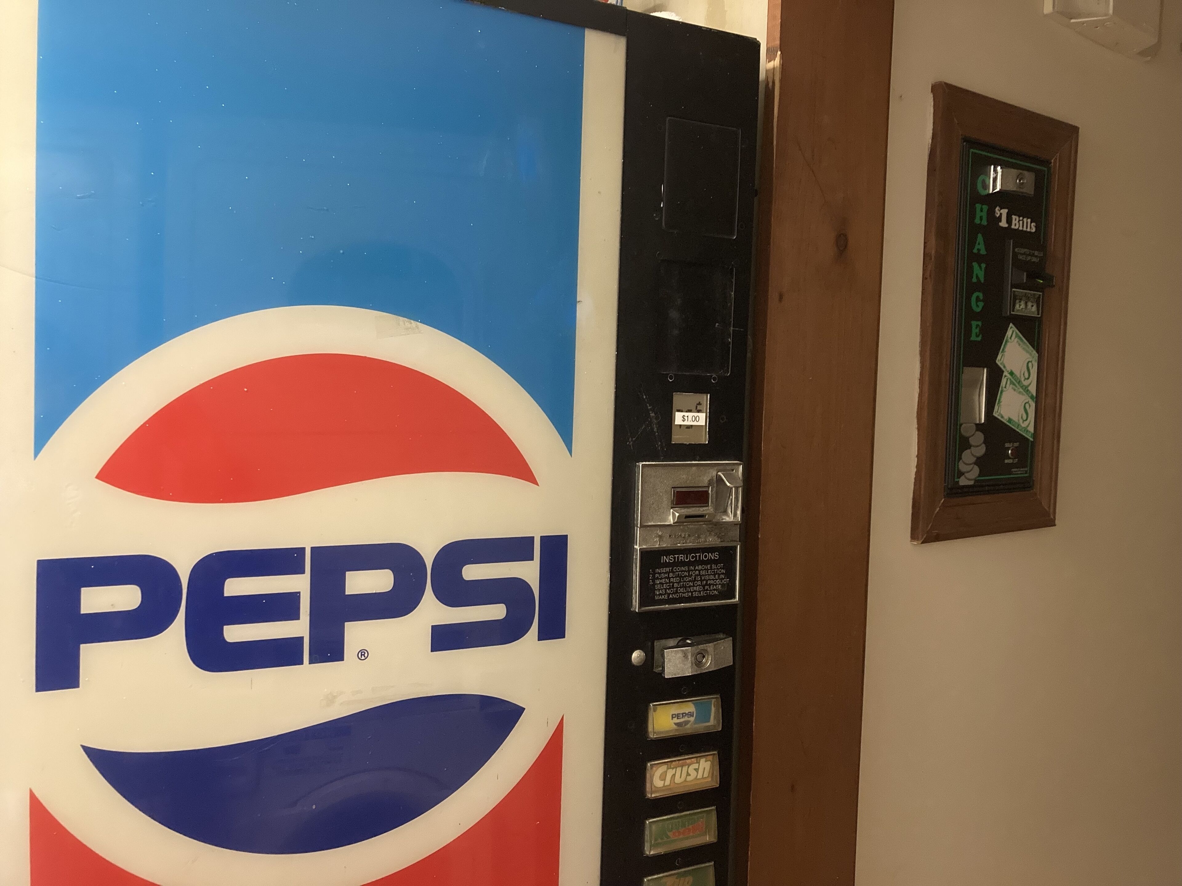 Una máquina expendedora con el logotipo de Pepsi, una ranura para monedas e instrucciones.