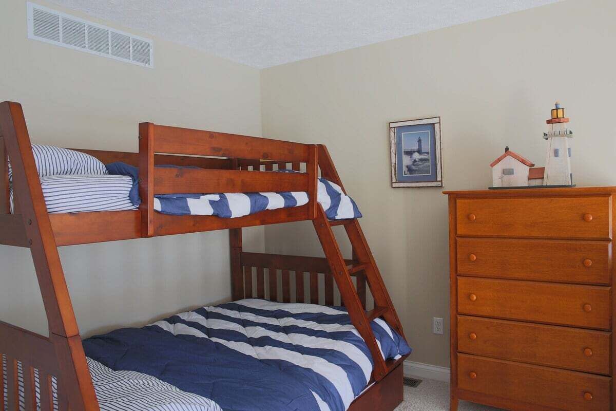 Una cama litera con ropa de cama a rayas, un aparador con cajones y un cuadro en la pared.