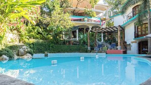 A swimming pool with a stone border, surrounded by lush greenery and a multi-story building with balconies. - Hotel Paraiso Encantado (Xilitla)