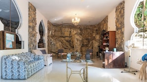 A spacious living room with a stone wall, a chandelier, a sofa, a coffee table, and a bookshelf. - Hotel Paraiso Encantado (Xilitla)