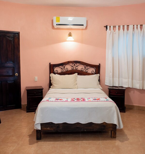 A bedroom with a wooden bed, white bedding, a wall-mounted air conditioner, and a window with white curtains. - Hotel Paraiso Encantado (Xilitla)