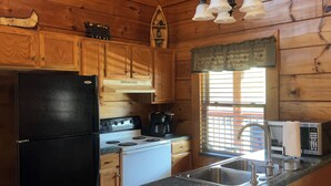 Una cucina con mobili in legno, un frigorifero nero, un fornello, un forno a microonde e un lavello.