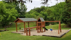 Un'area giochi in legno con scivolo, altalene e tavoli da picnic.