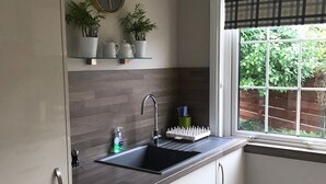 A modern kitchen with a black sink, white cabinets, a clock, and a window with a view of greenery. - Apartment 101 Kingsmills Road (Inverness)