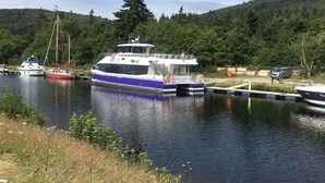 A river with boats docked, surrounded by greenery and a forested hill. - Apartment 101 Kingsmills Road (Inverness)